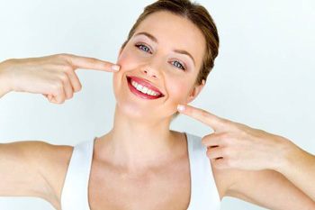 A woman smiling and pointing to her mouth