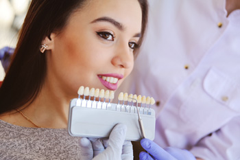 Woman smiling with dentist holding shade guide to her teeth