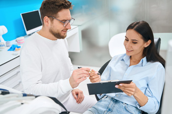 Woman in dental chair signing forms on clipboard to hand to dentist