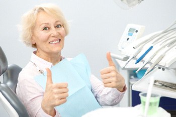 Senior woman sitting in dental chair giving two thumbs up