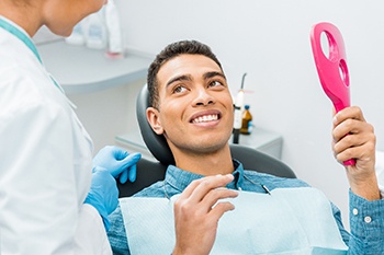 Man smiling at dentist while holding small mirror