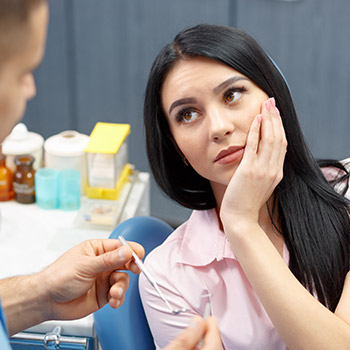 Woman in dental chair holding cheek