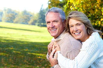 An older couple smiling and hugging outside.