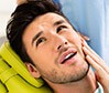 Man in dental chair holding cheek in pain