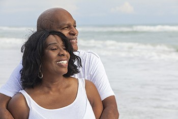 An older couple smiling and hugging at the beach.