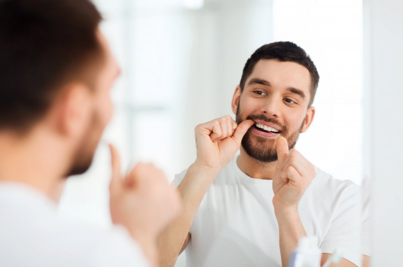 Young man flossing in the mirror