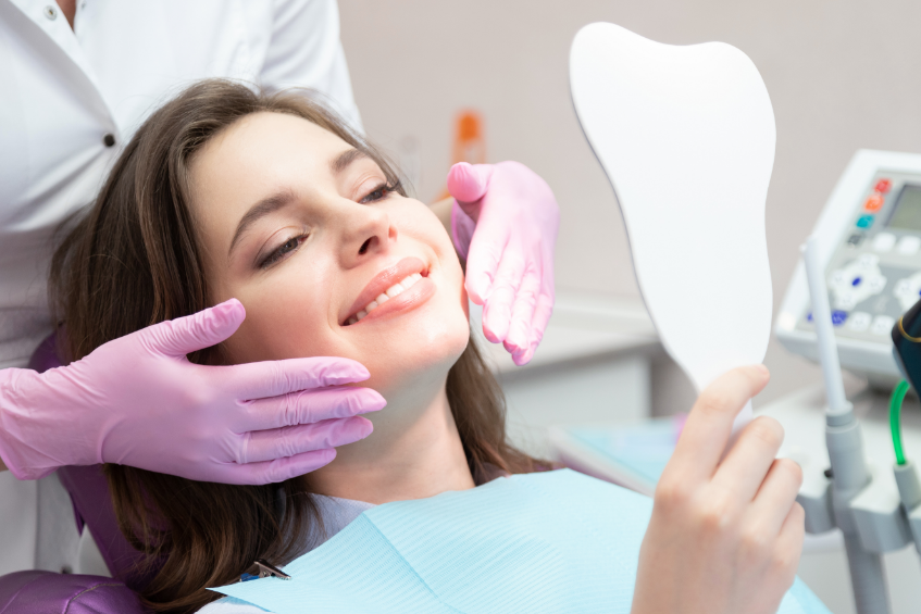 Woman smiling from dental chair and holding mirror